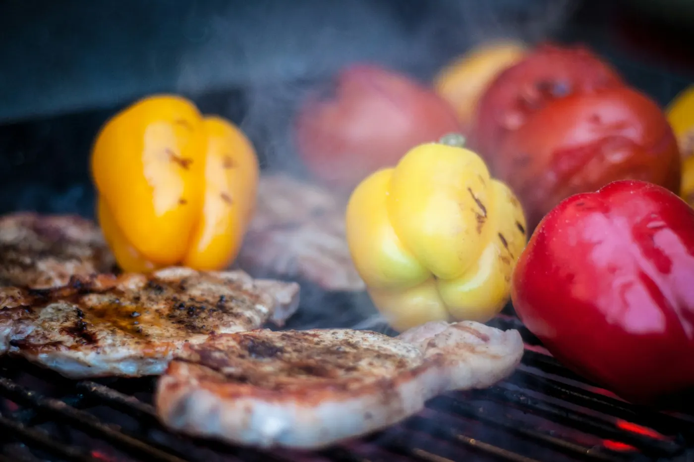 Whole peppers and cuts of meat cooking over a grill