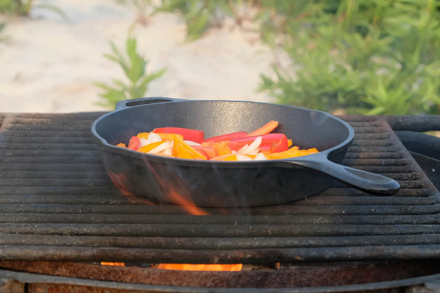 Peppers and onions cooking in a cast iron skillet over an open flame