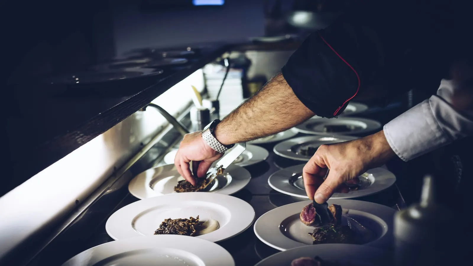 Hands plating several dishes at once on a restaurant pass