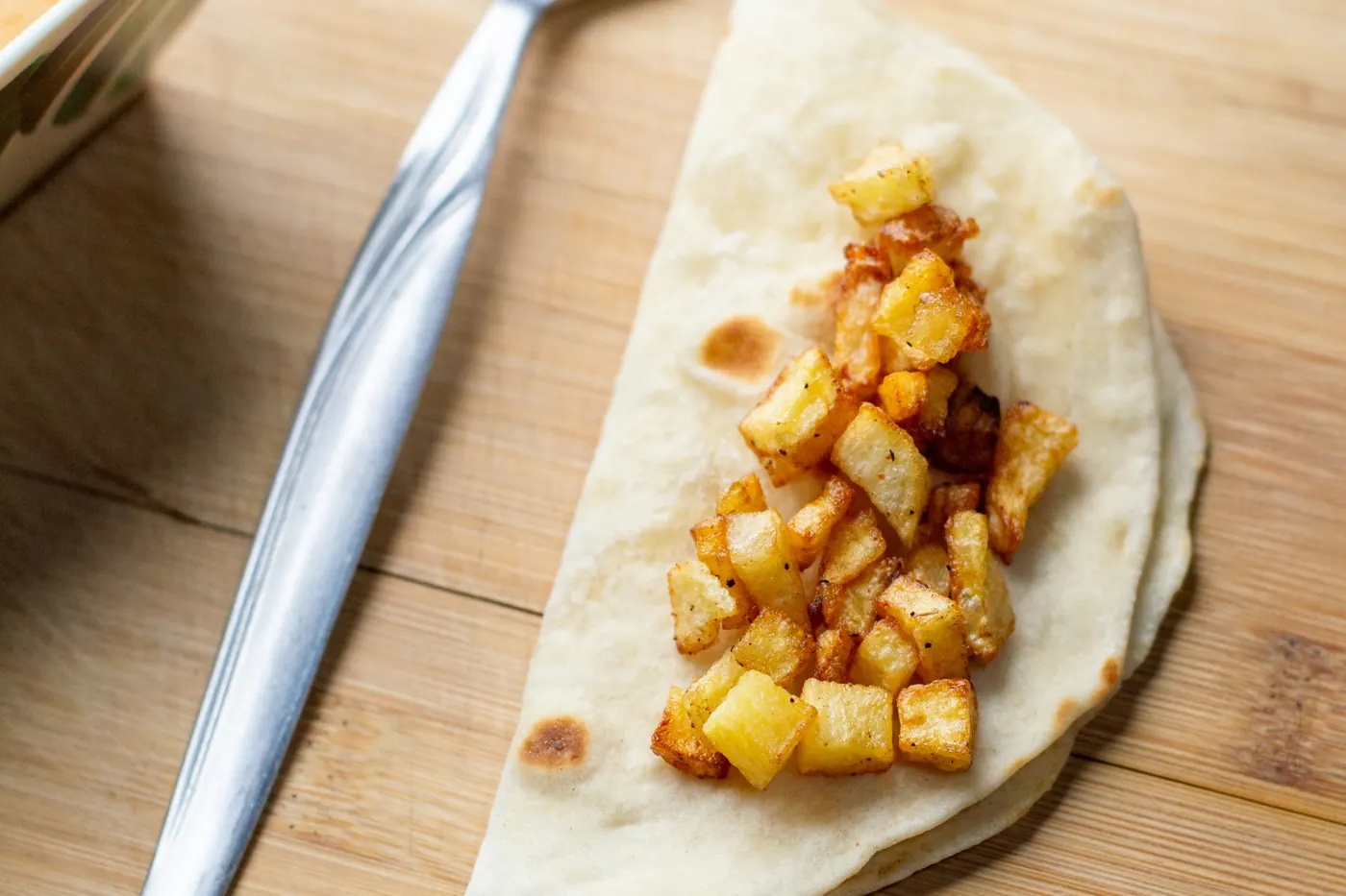 Diced potato on an open flour tortilla with a fork beside it