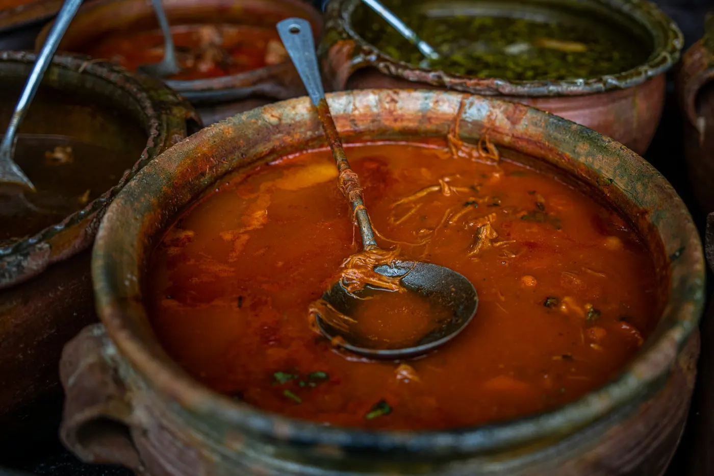Clay pots of red and green sauces side by side at a market