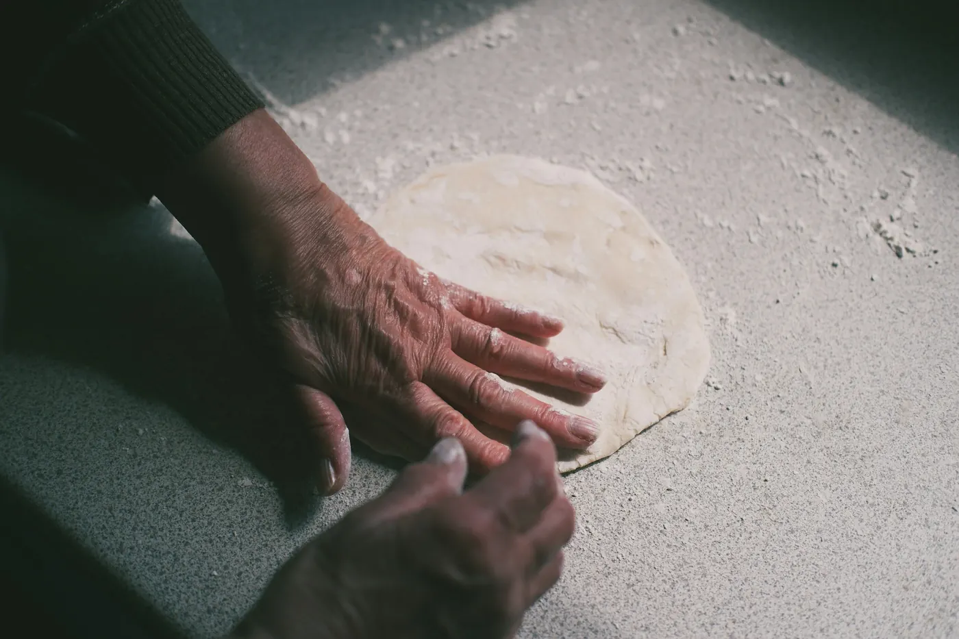Hands pressing out a round of tortilla dough on a floured surface