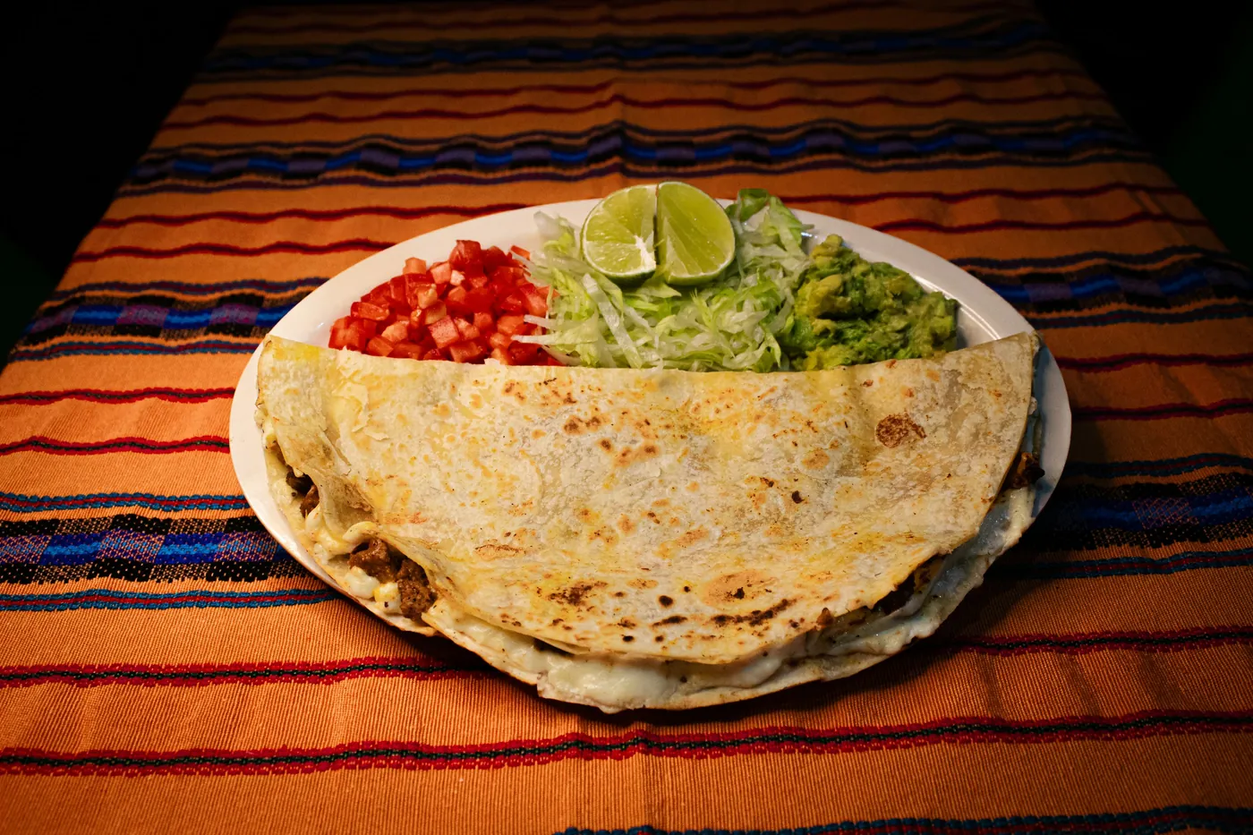 A folded quesadilla served with guacamole and salsa on a striped cloth