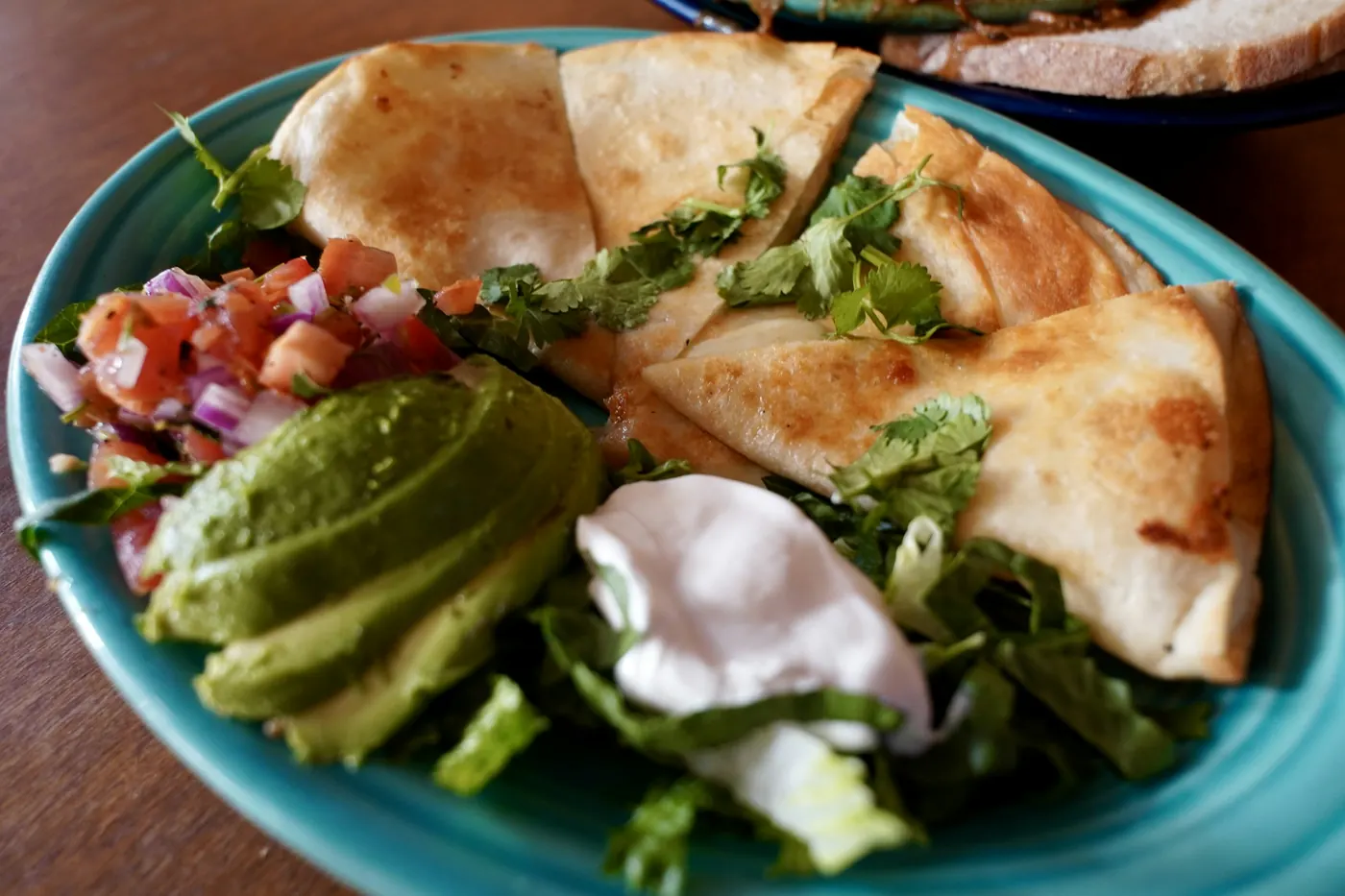 A quesadilla plated with avocado, pico de gallo and sour cream