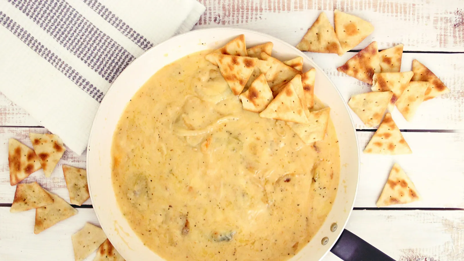 A bowl of smooth pale cheese dip surrounded by tortilla chips