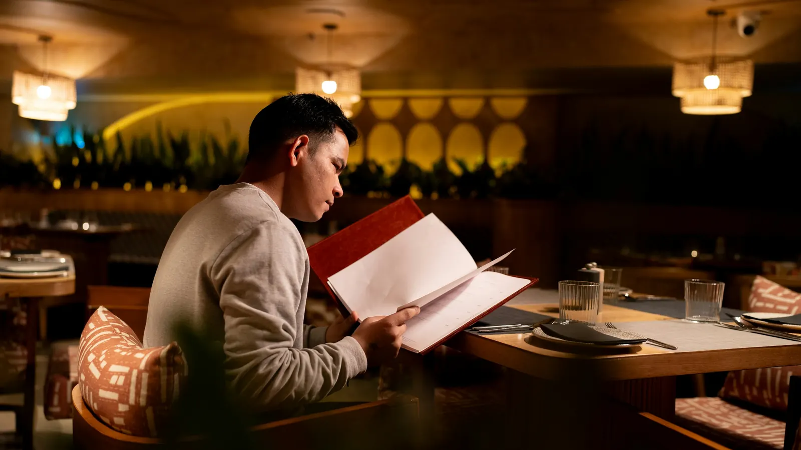 A person reading a menu at a table in a warmly lit restaurant