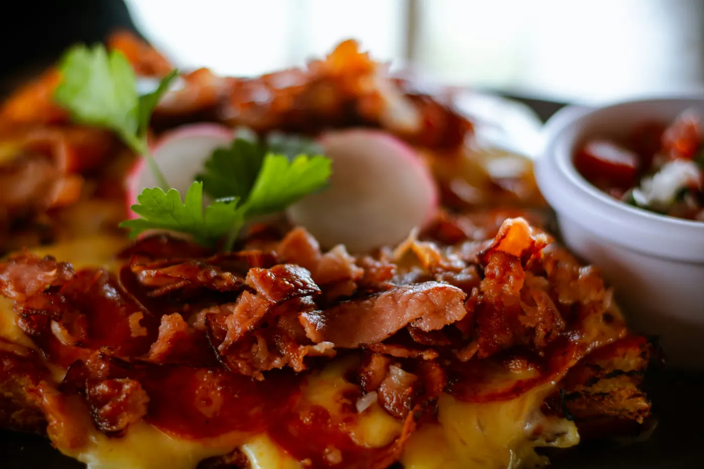 Tortilla pieces coated in red sauce under melted cheese and herbs