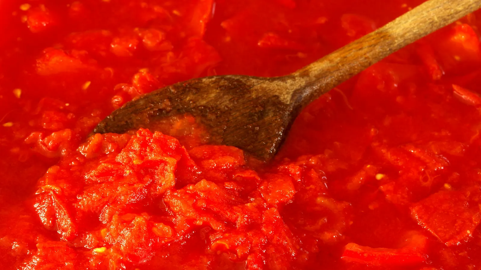A wooden spoon stirring a thick red sauce