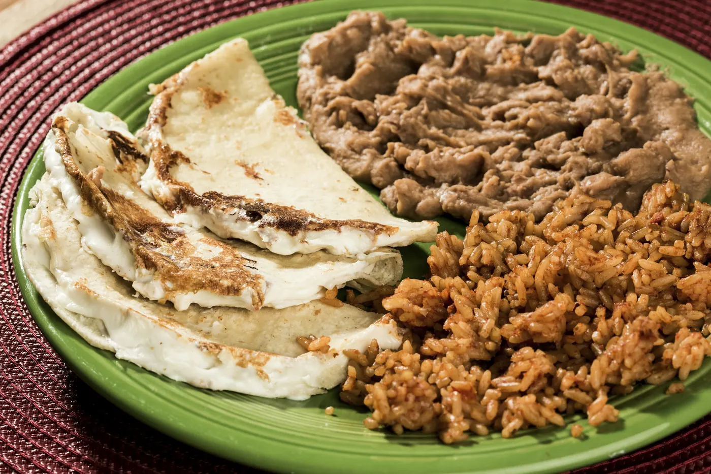 A green plate holding refried beans and folded tortillas