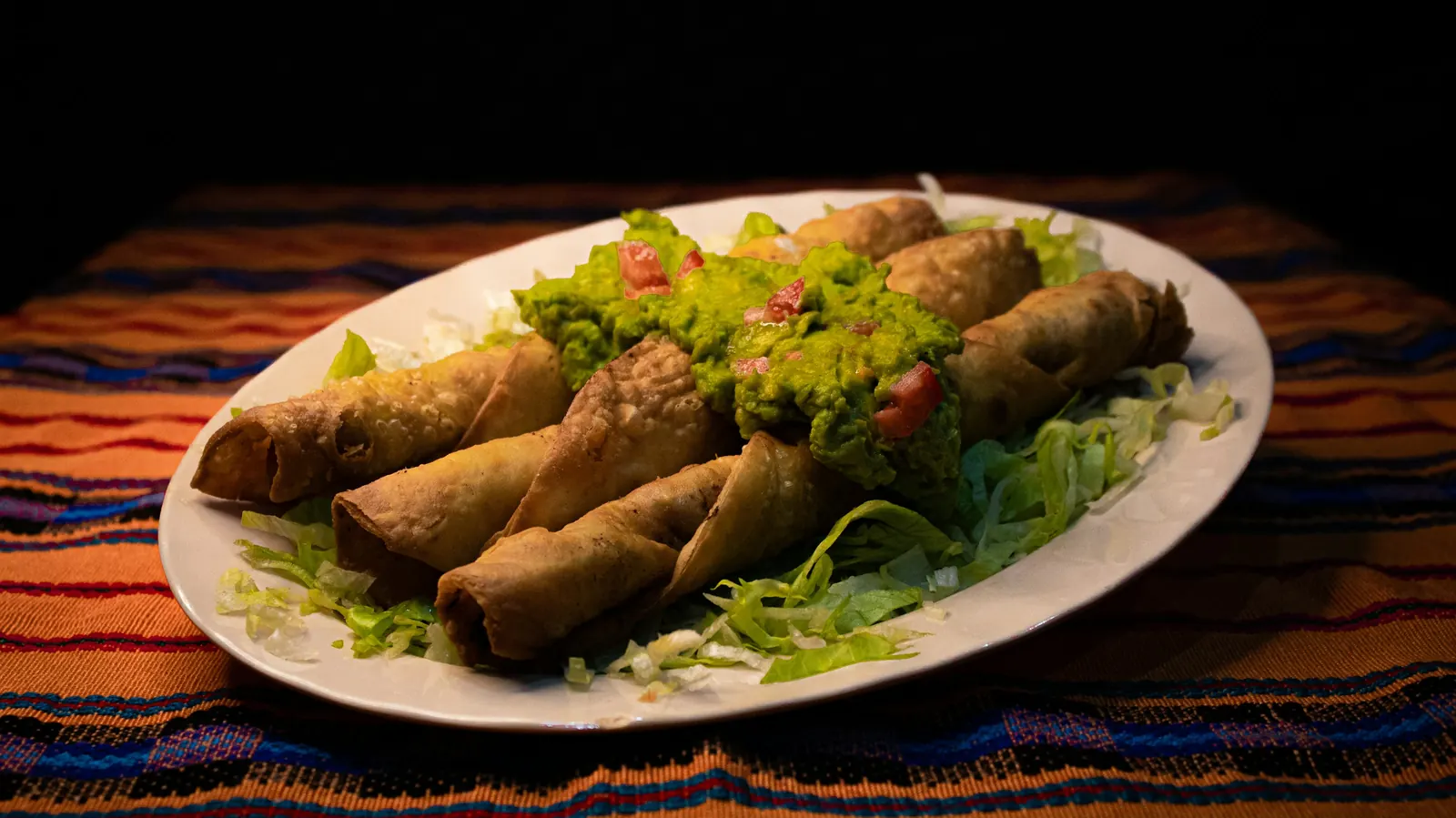 Several rolled and fried tortillas on a plate with lettuce and guacamole