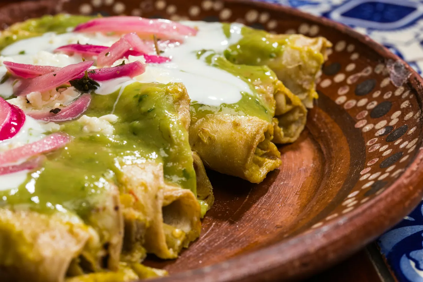 Rolled tortillas covered in green sauce with cream and pickled onion