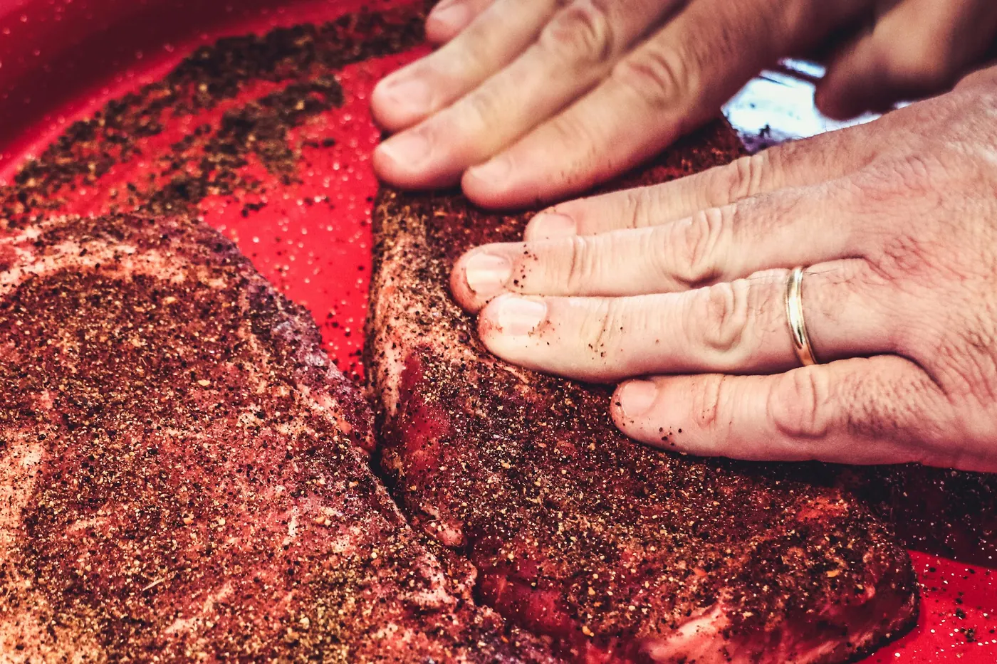 Hands working a red seasoning paste into a cut of meat