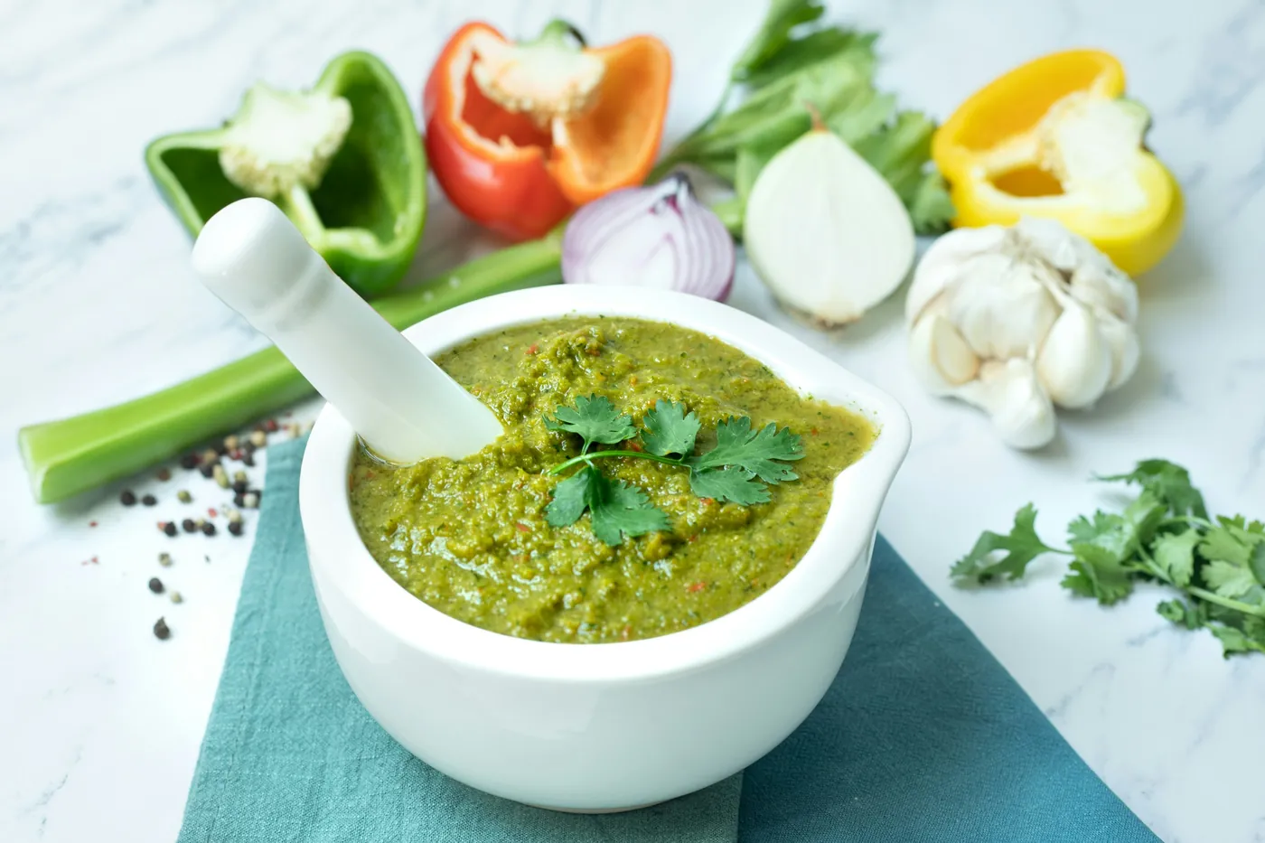 Green tomatillo salsa in a white mortar surrounded by fresh peppers and garlic