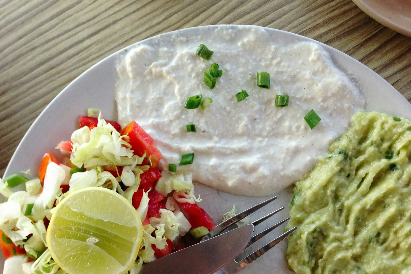 A plate of scrambled eggs with tomato, avocado and lime