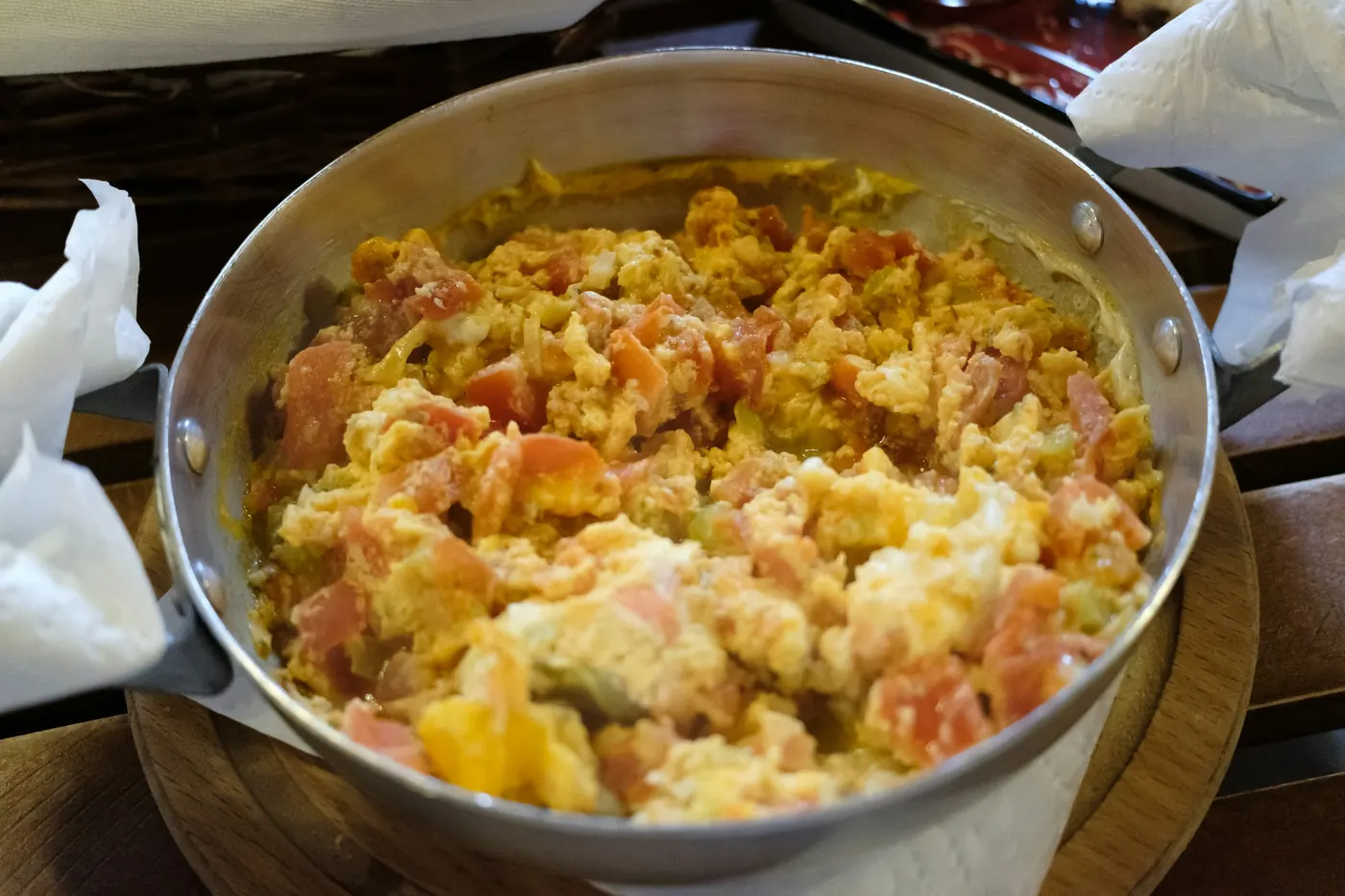 Scrambled eggs cooked with chopped tomato in a metal pan