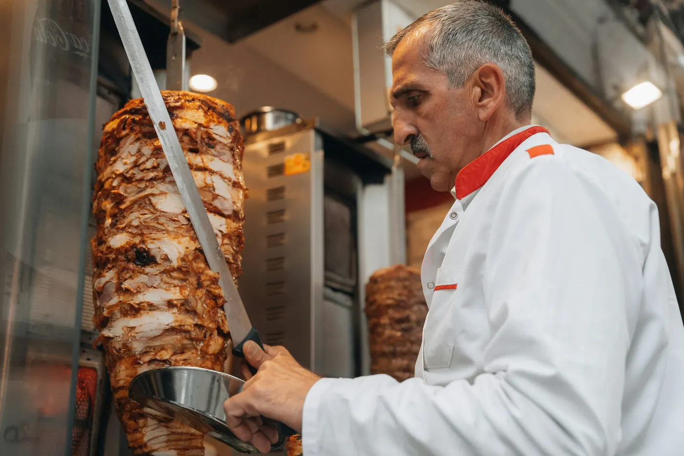 A cook slicing down a vertical rotisserie with a long knife