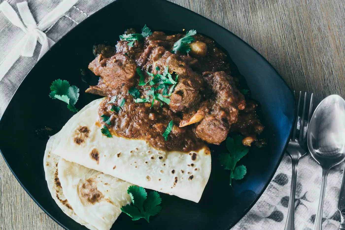 Shredded braised beef on a dark plate served with soft tortillas