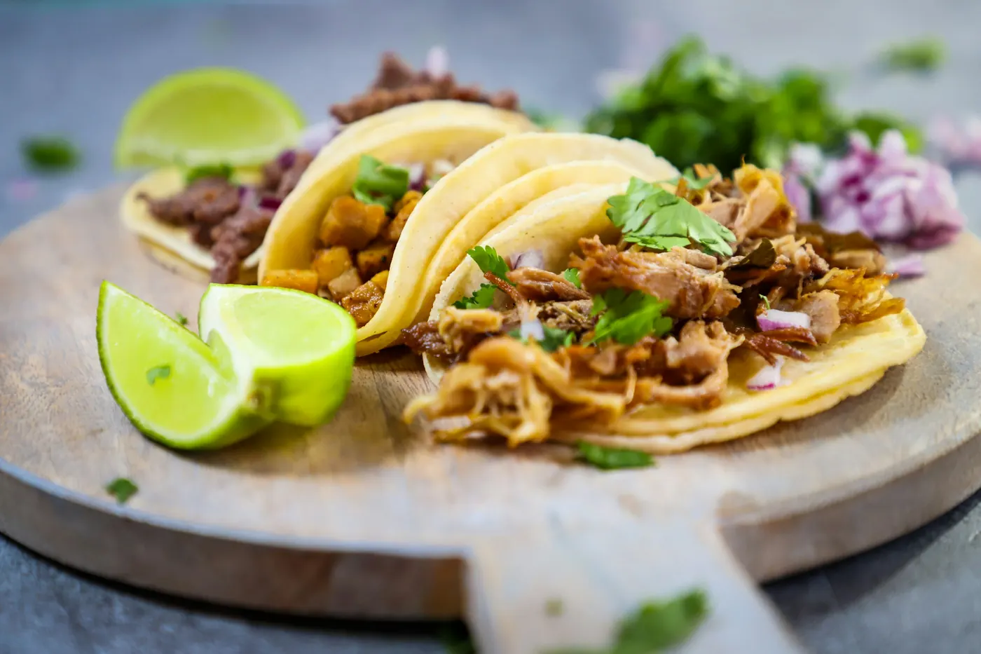 Tacos filled with shredded meat and cilantro on a round wooden board