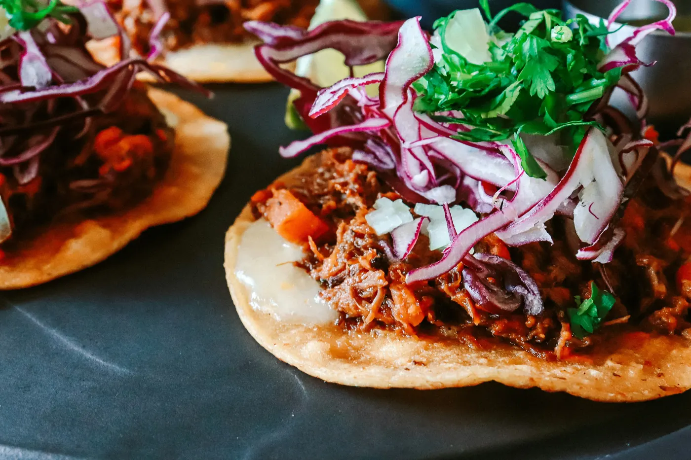 A tostada topped with shredded meat and bright pink pickled onion