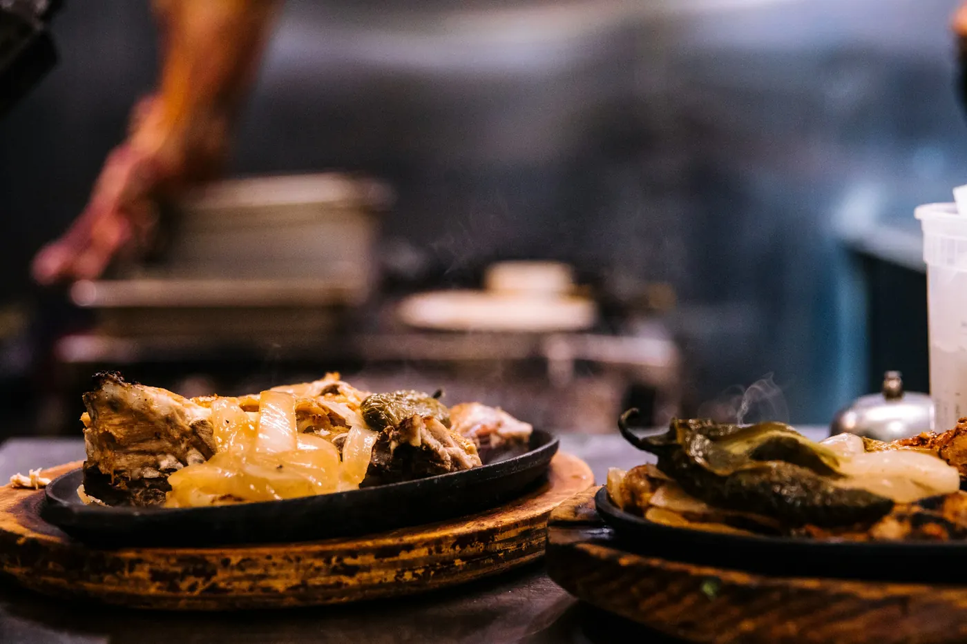 Cast iron plates of grilled meat steaming as they leave a restaurant kitchen