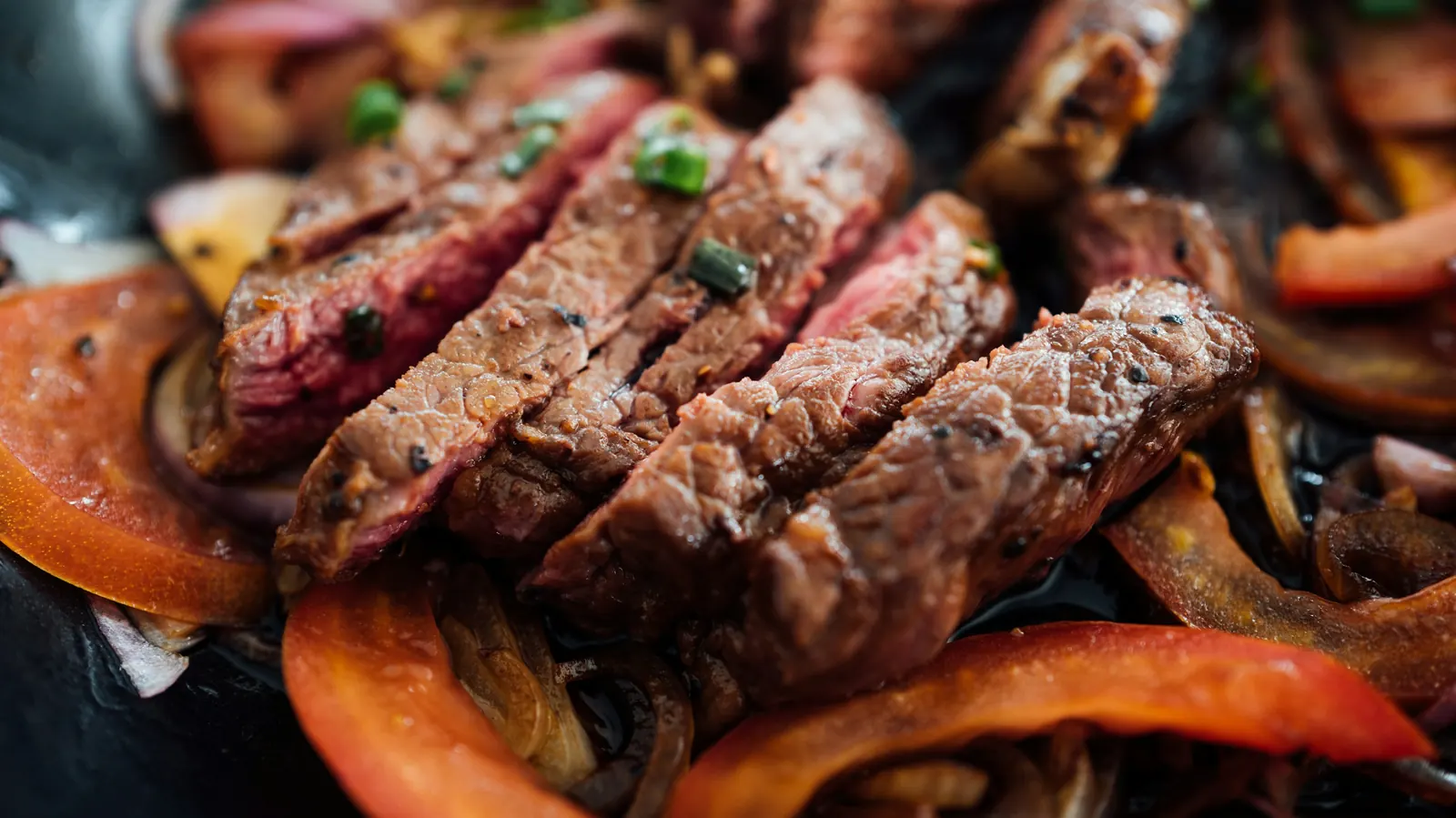 Sliced grilled steak with charred red peppers and onion