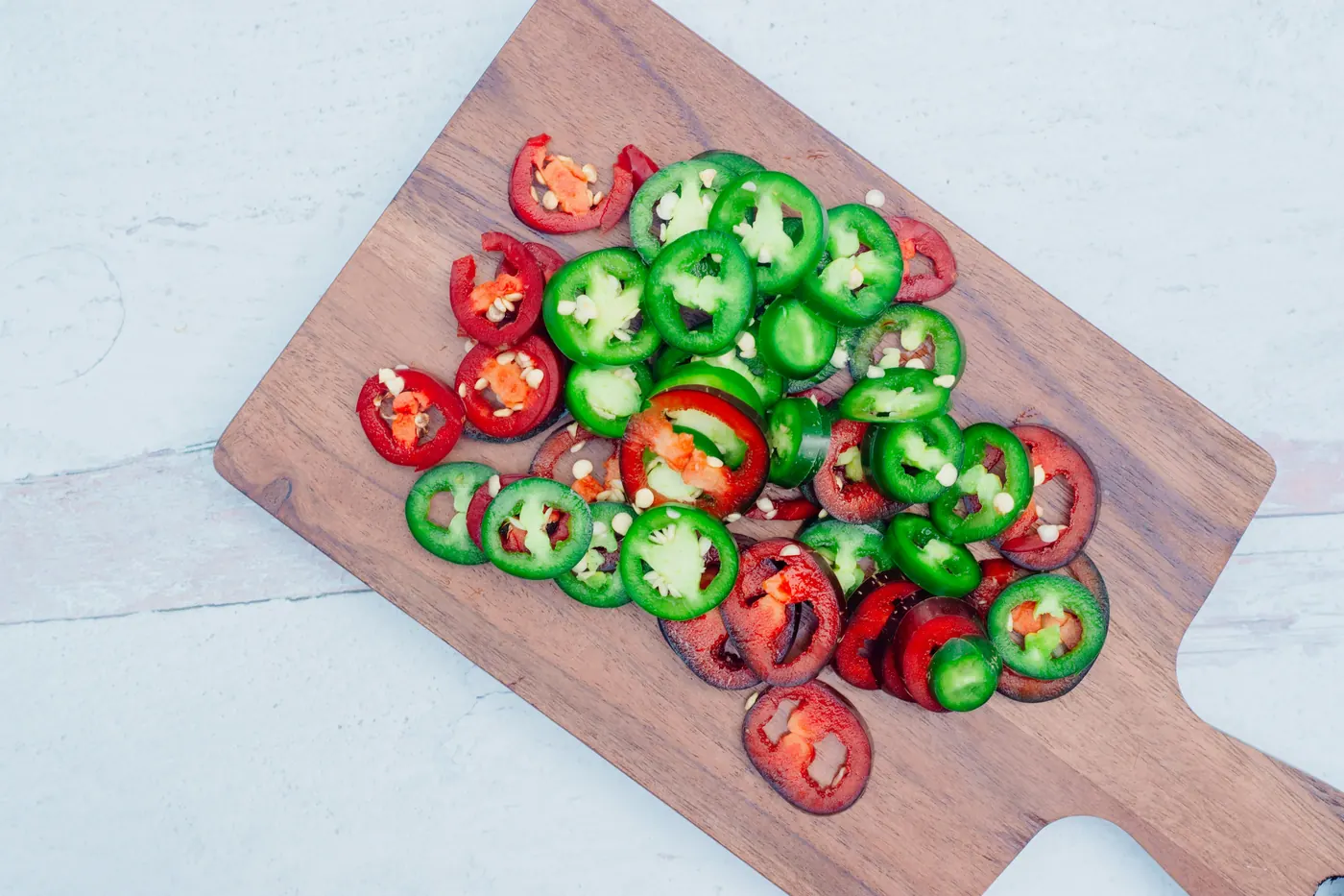 Sliced red and green jalapenos arranged on a wooden board