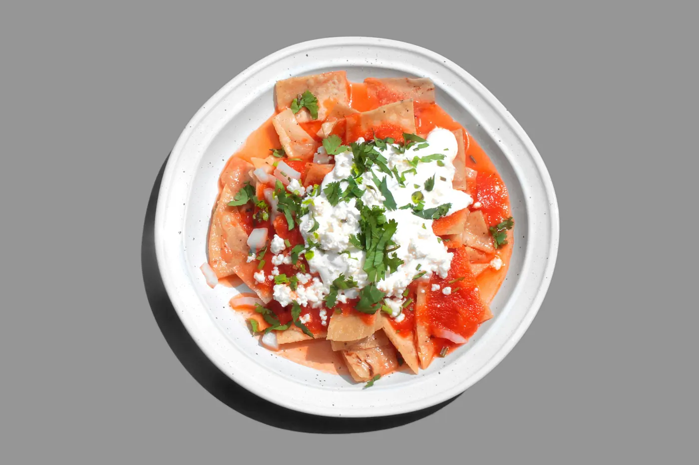 Sliced tomato on a white plate scattered with crumbled white cheese and herbs