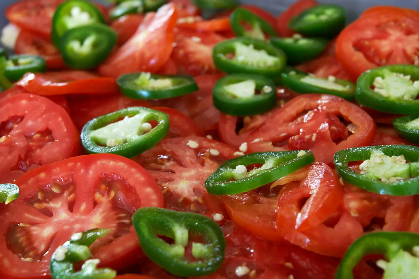 Sliced tomato scattered with rings of green jalapeno