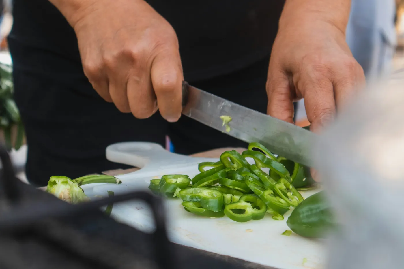 A knife slicing a green chile into thin rings