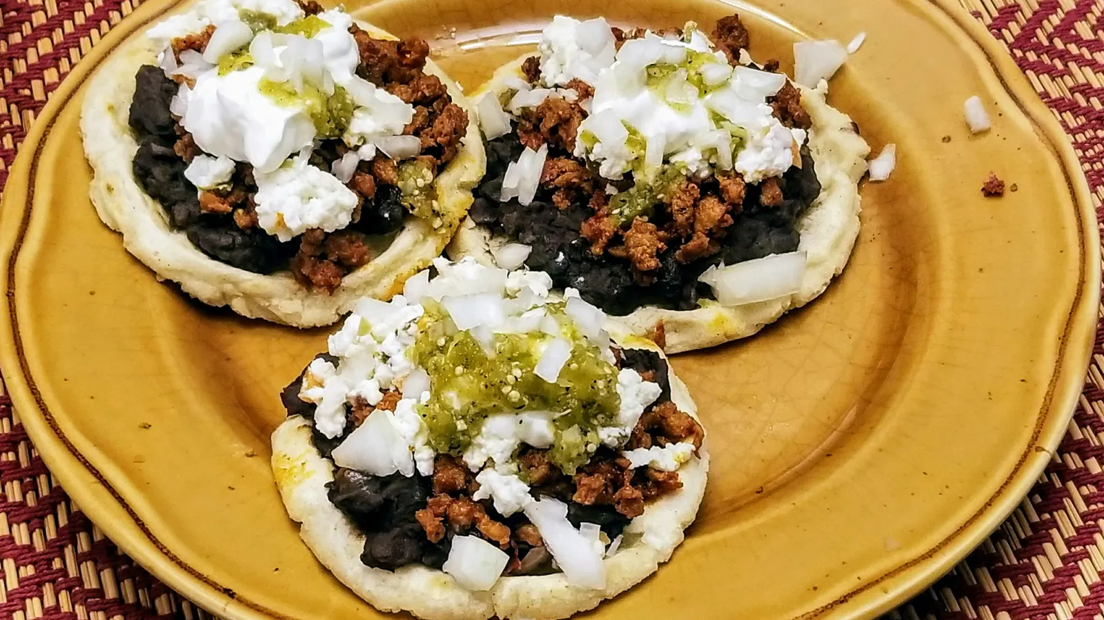 Three thick masa cakes topped with beans, shredded meat, crema and cheese