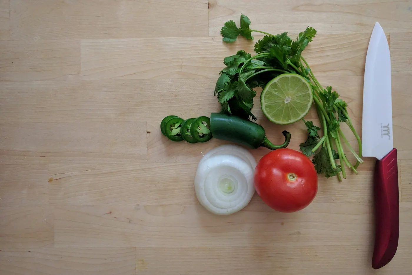 Cilantro, lime, jalapeno, onion and tomato arranged on a wooden board