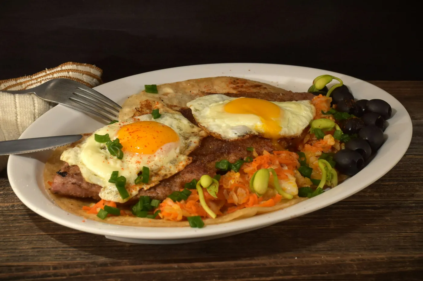 Grilled steak served with fried eggs, black beans and salsa