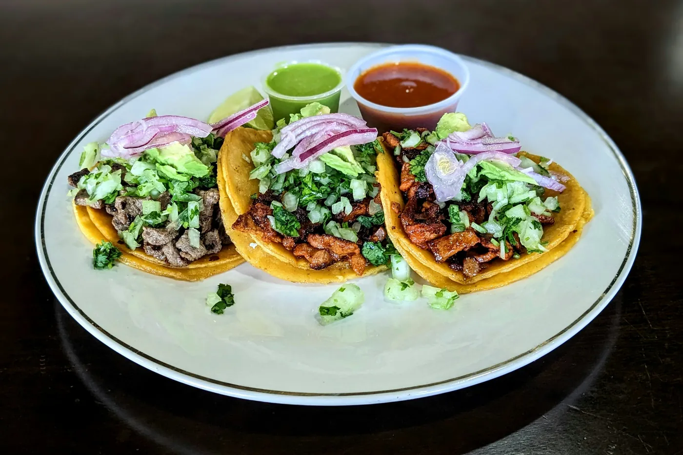 Three street tacos on a white plate served with two salsas