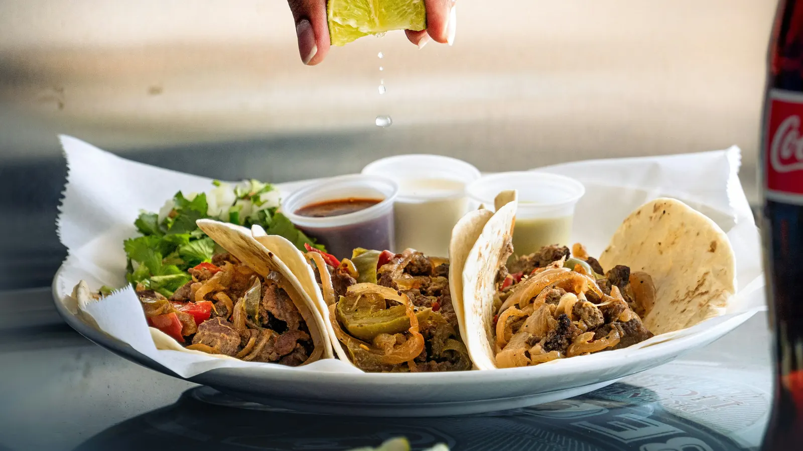 Three street tacos on a plate with lime being squeezed over them