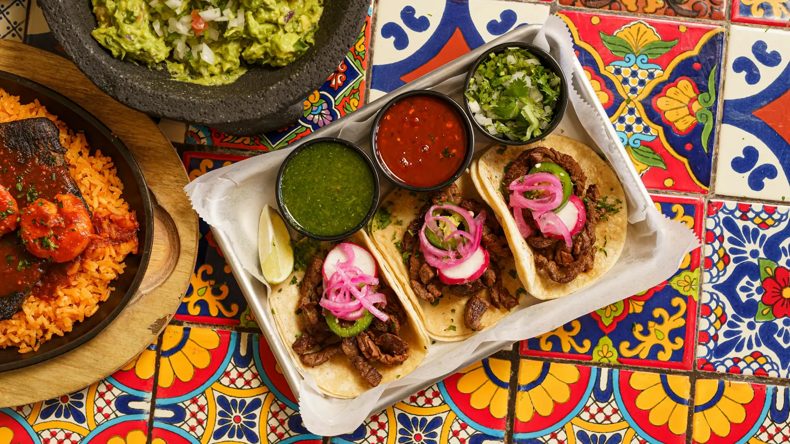 An overhead view of a taco platter with bowls of salsa on a tiled table