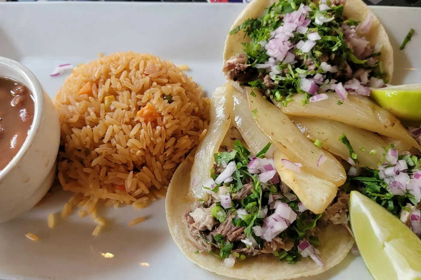Tacos served on a plate with Mexican rice and a bowl of charro beans
