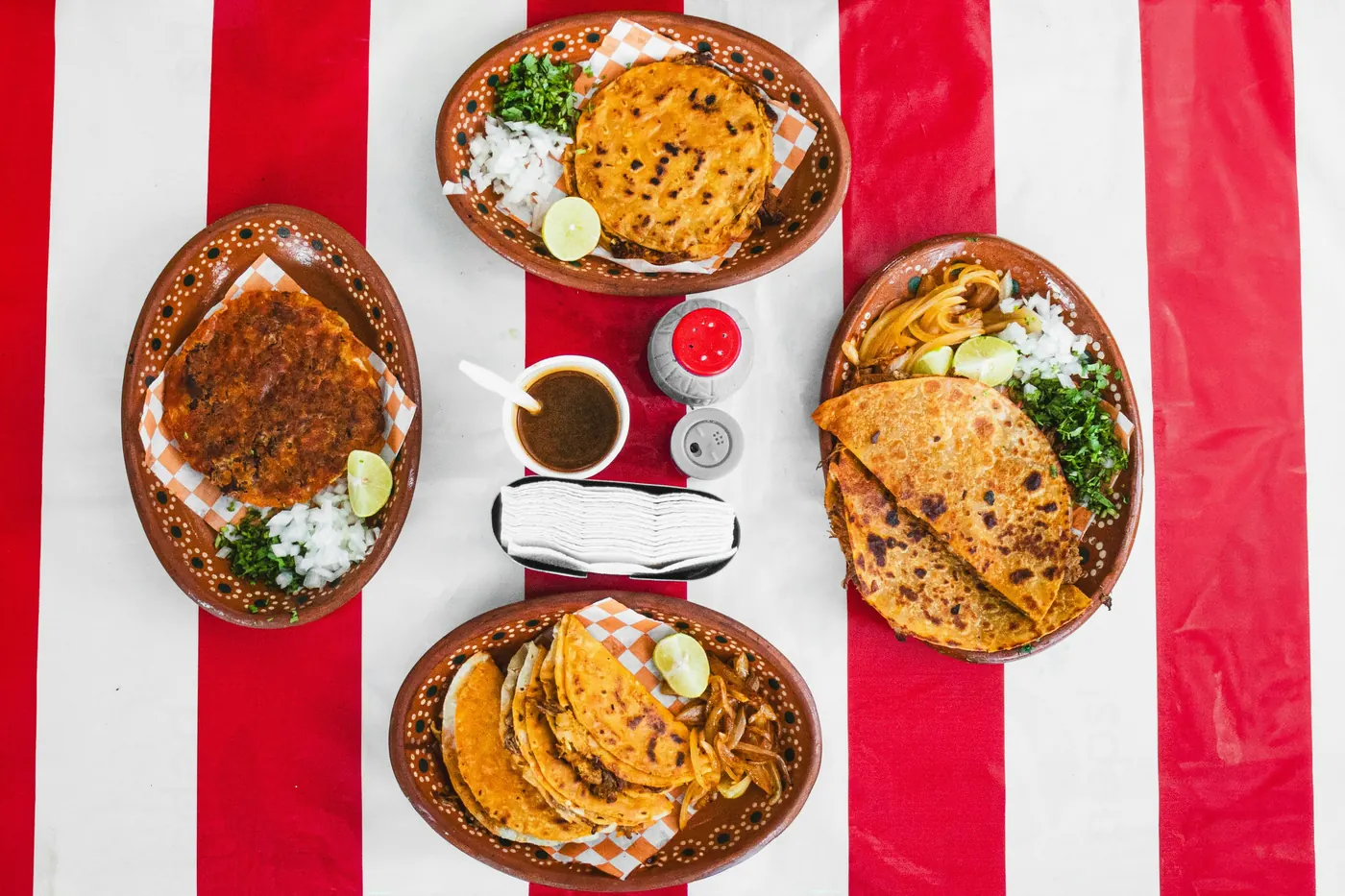 Three small clay dishes each holding a different topped masa antojito