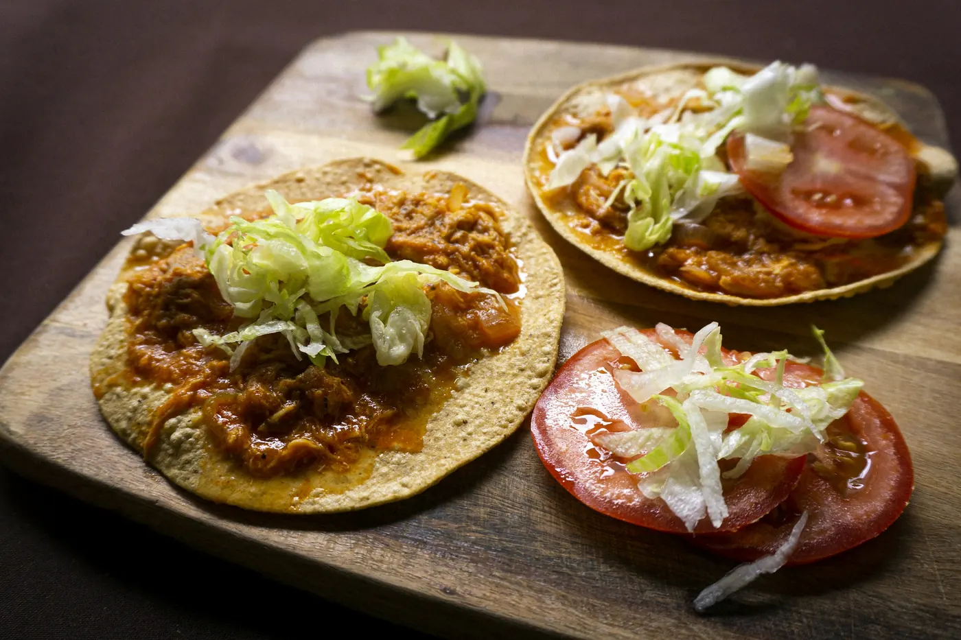 Topped masa cakes with meat, lettuce and tomato on a wooden board