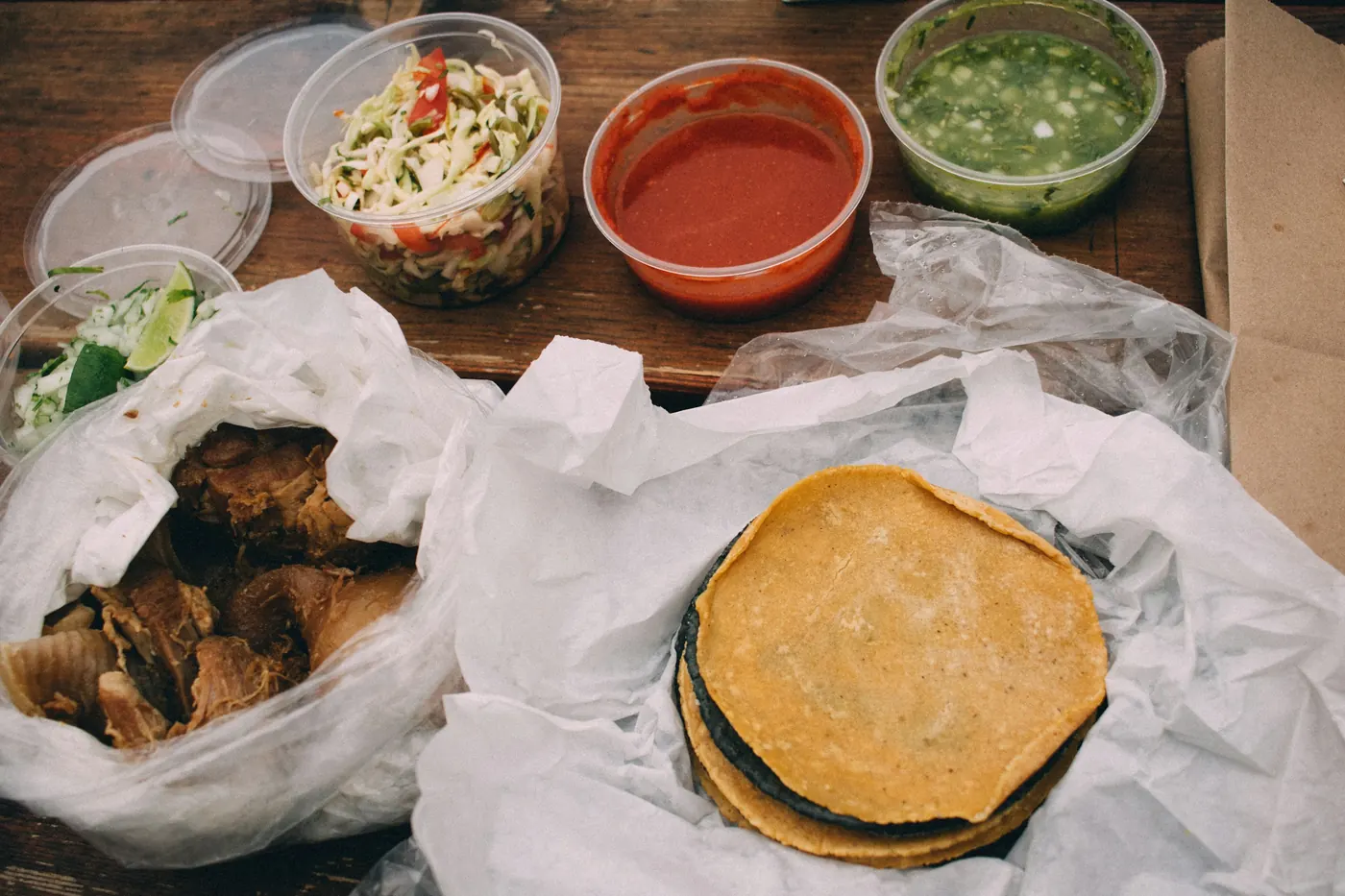Warm tortillas and meat in paper beside bowls of salsa
