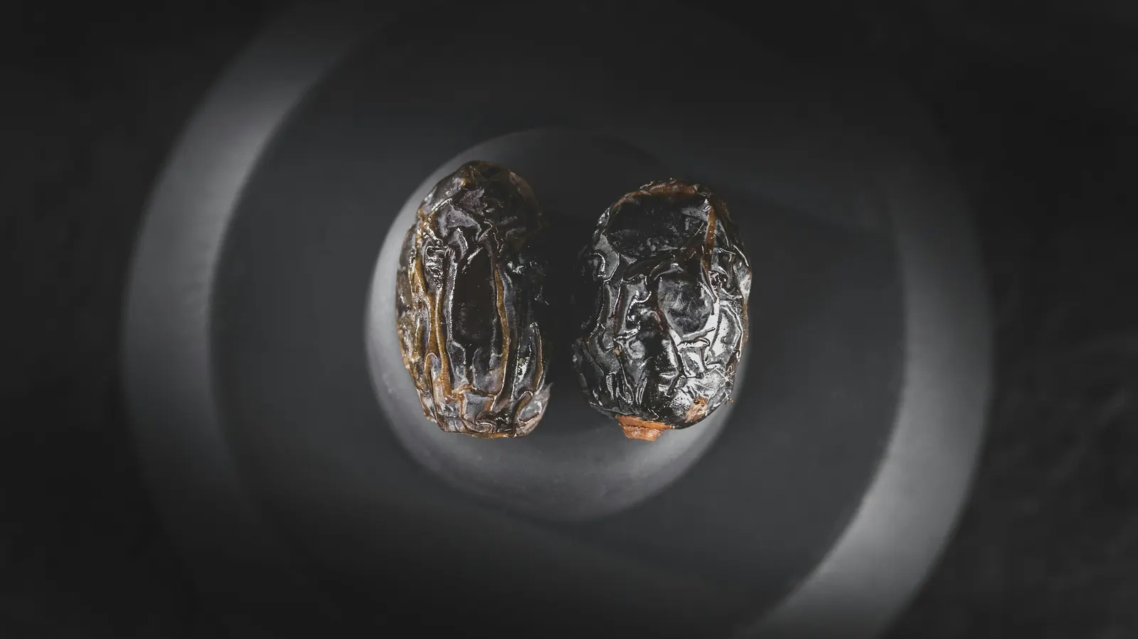Two dark, wrinkled dried chiles against a dark background