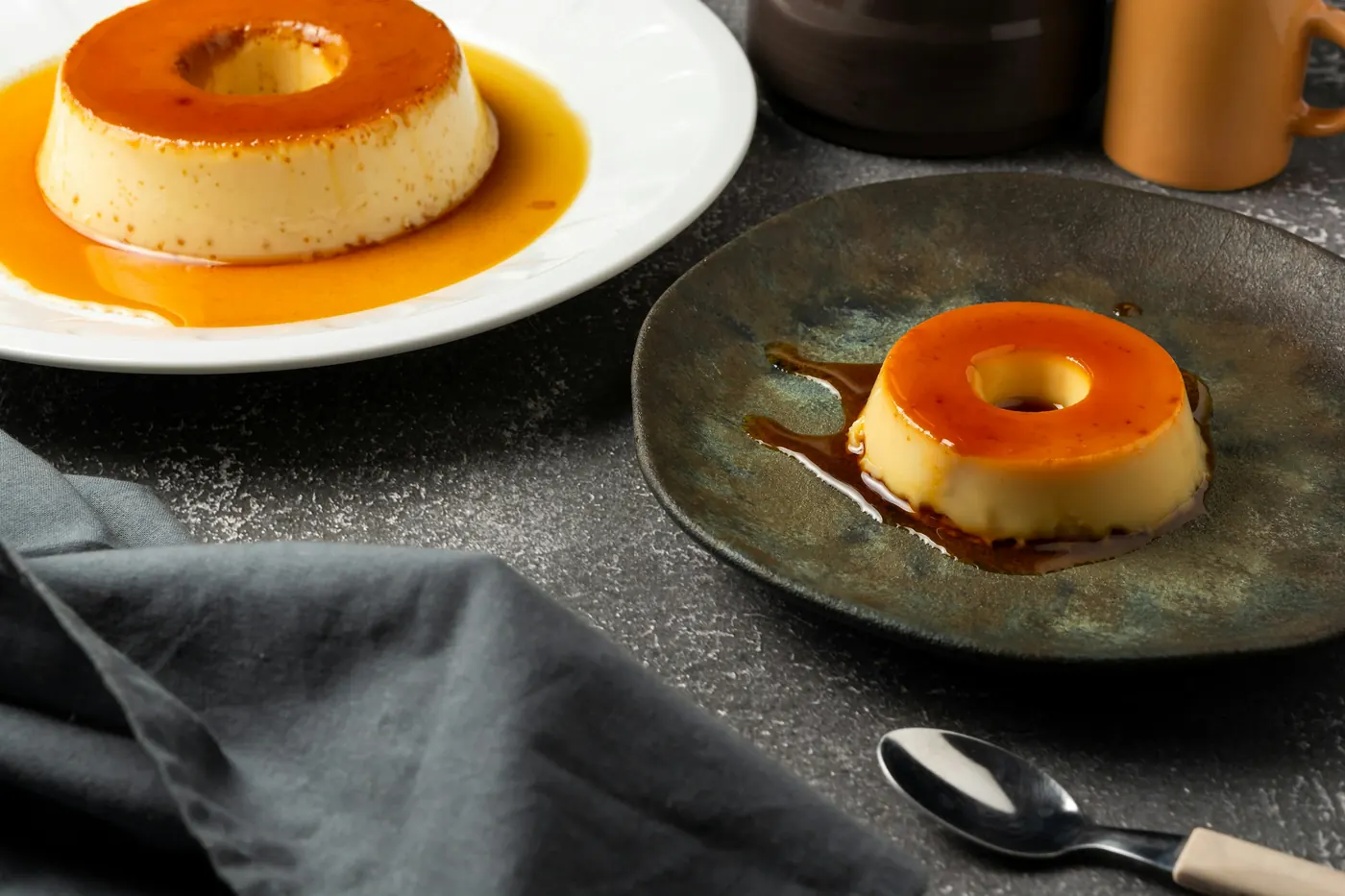 Two portions of set custard on plates with a spoon and folded napkin