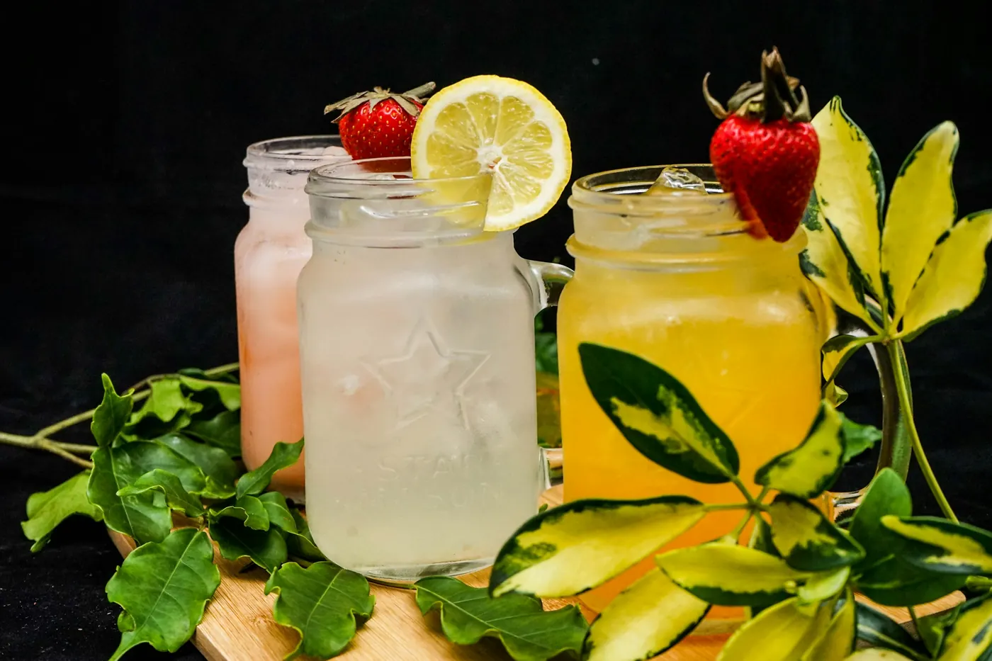 Two mason jars of pale and yellow drink garnished with citrus