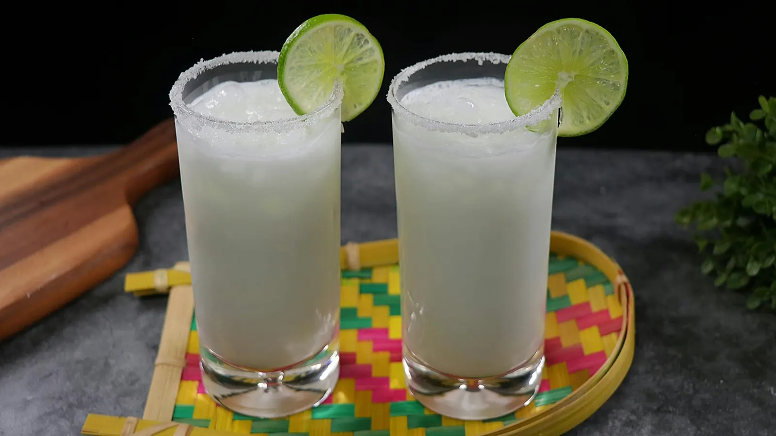 Two tall lime margaritas with salted rims on a woven table mat