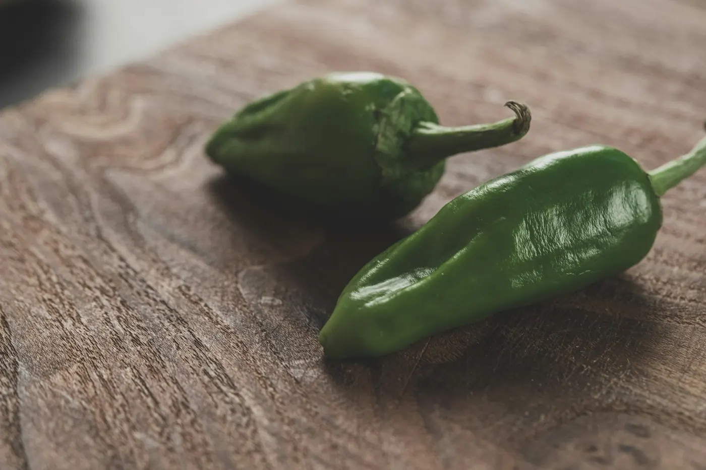 Two thick-walled dark green chile peppers on a wooden surface