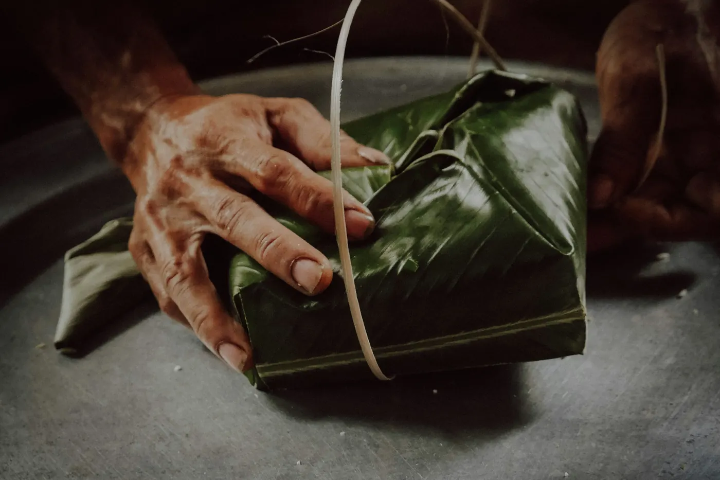 Hands tying string around a leaf-wrapped parcel