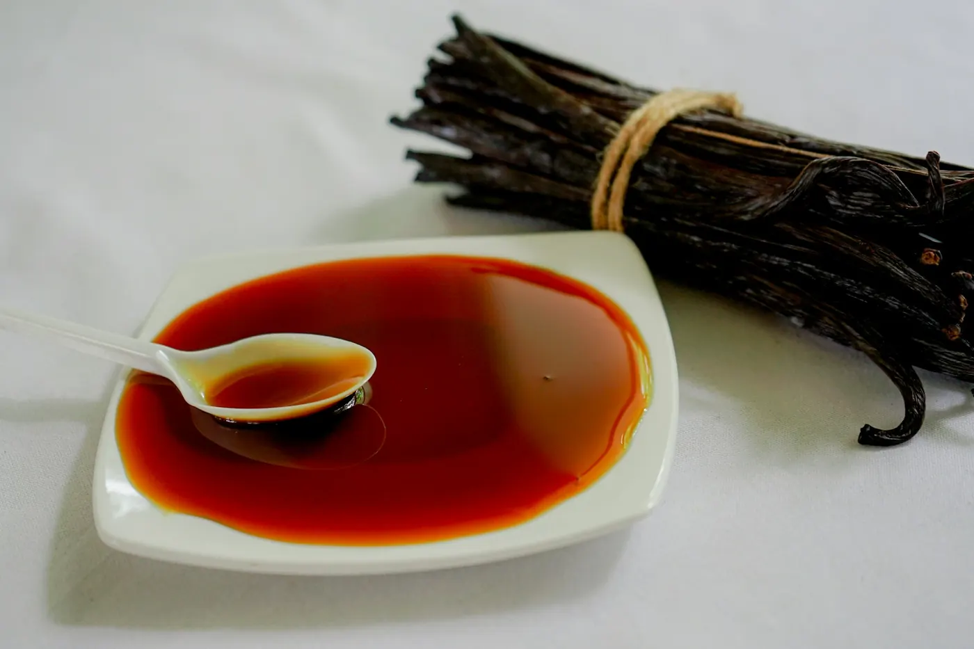 A bundle of vanilla beans beside a white dish of dark liquid extract