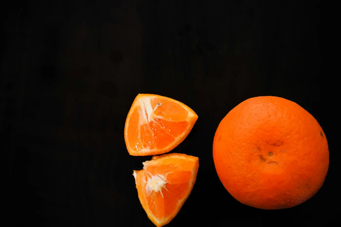 A whole orange beside peeled segments on a dark surface