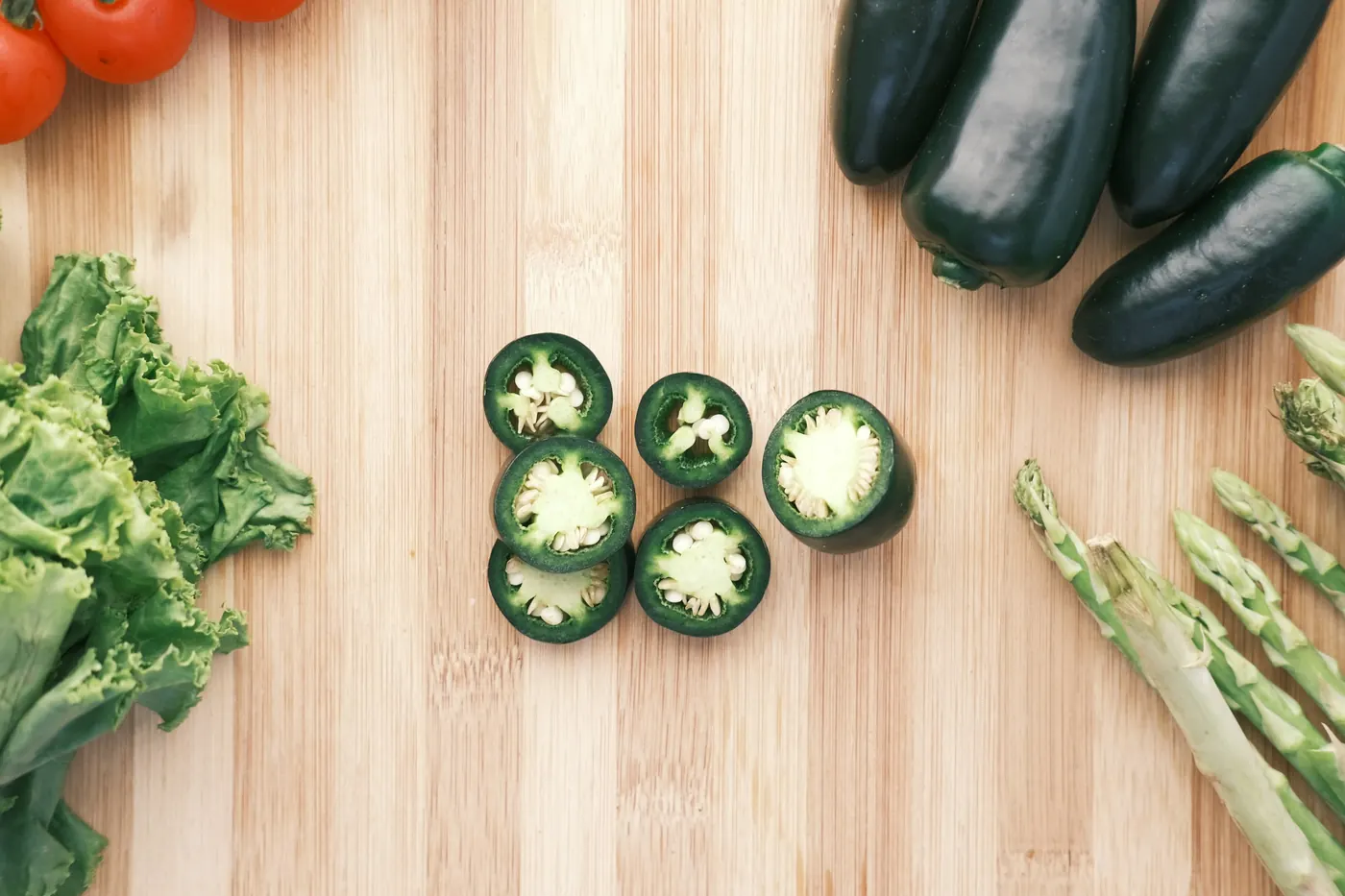 Whole and sliced jalapeno peppers on a wooden board showing the seeds inside