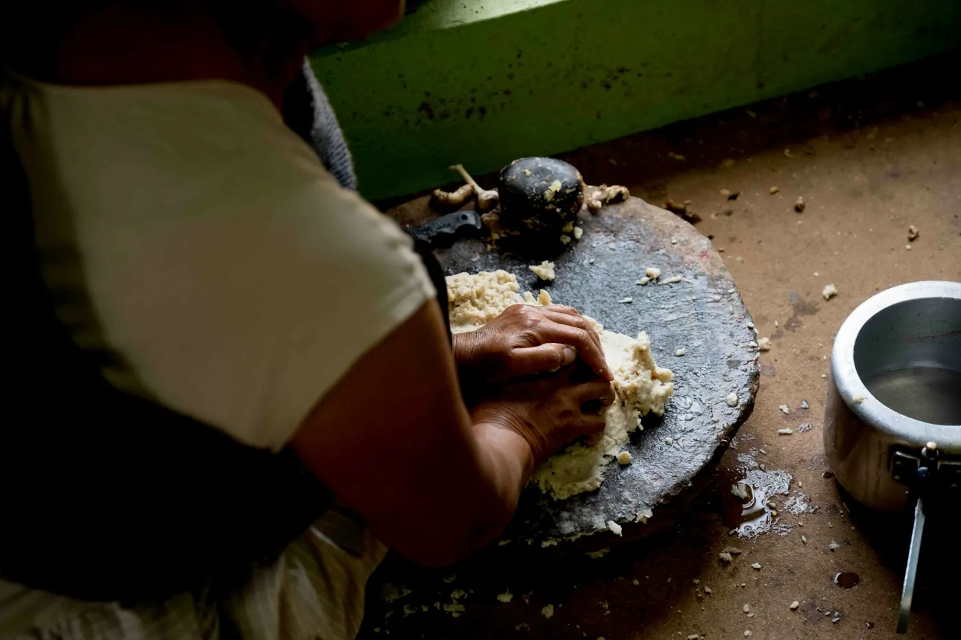 Hands working corn masa on a stone beside a griddle
