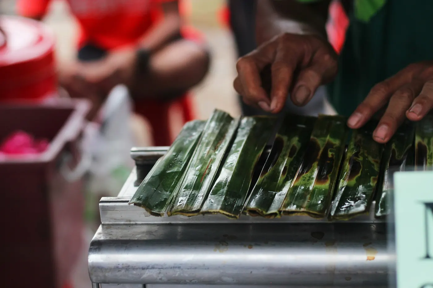 Hands wrapping food into green leaf parcels on a metal counter